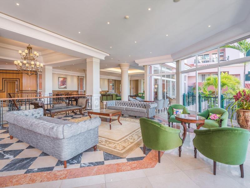 Lounge dell'hotel luminosa con divani comodi, poltrone e grandi finestre sul giardino.