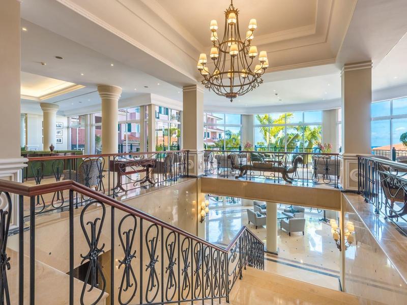 Lobby dell'hotel luminosa con scala, lampadario e area salotto con vista mare.