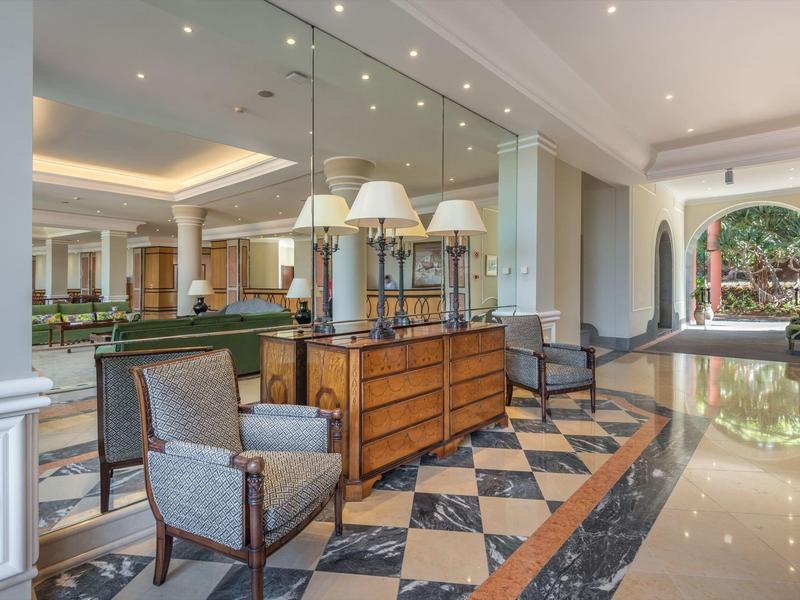 Elegante hall dell'hotel con poltrone imbottite, cassettiera in legno e specchio illuminato.