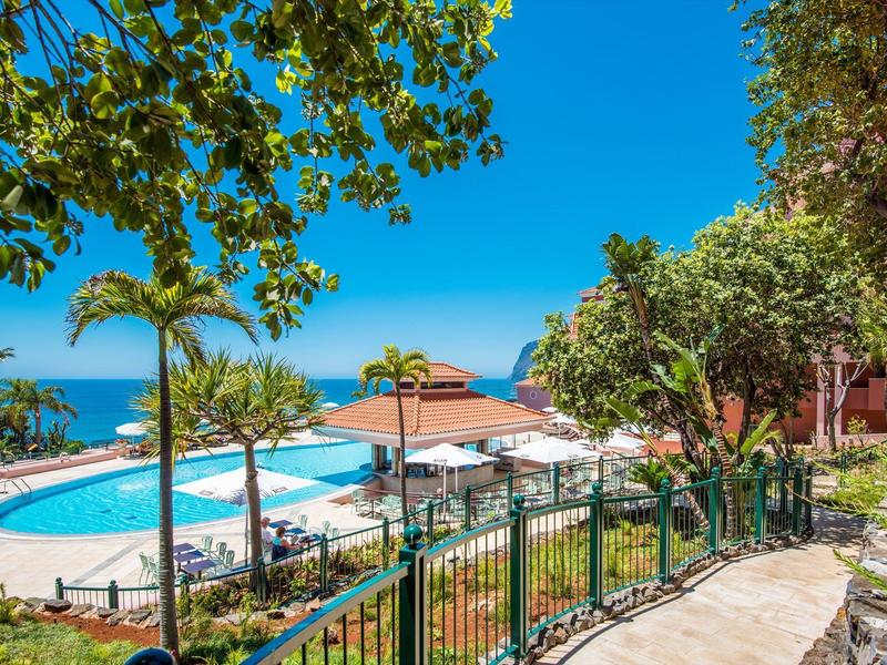 Area piscina con palme e vista sul mare sotto un cielo azzurro.