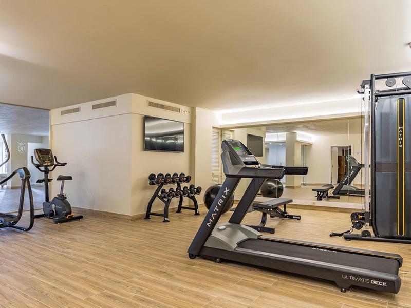 Palestra moderna con tapis roulant, cross trainer e pesi su pavimento in legno.