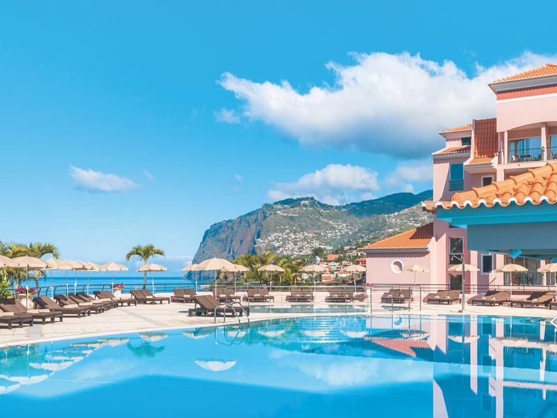 Piscina dell'hotel con lettini e vista mare sotto un cielo azzurro.