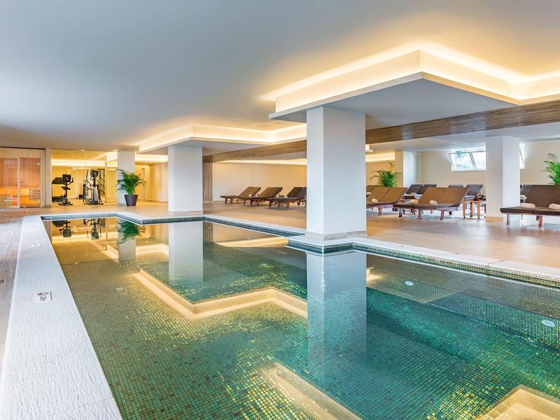 Piscina interna moderna con illuminazione elegante e aree relax confortevoli.