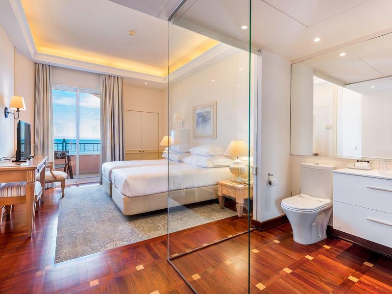 Camera d'hotel moderna con letto matrimoniale e bagno adiacente con parete in vetro.