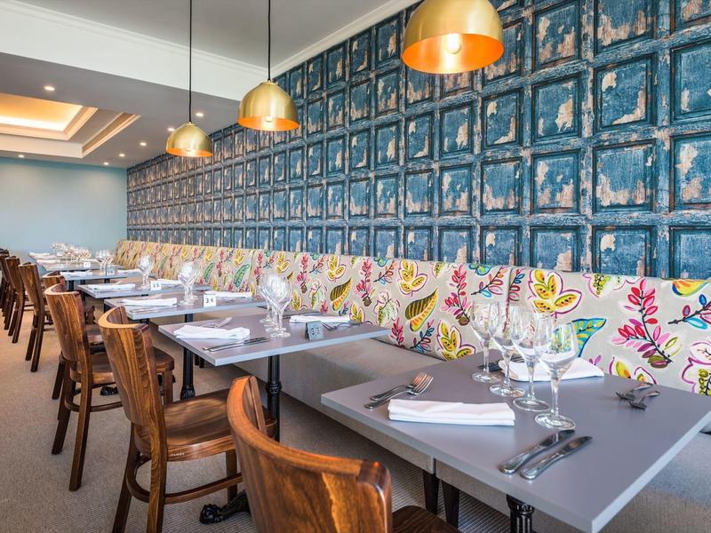 Area ristorante dell'hotel moderna con tavoli in legno e pannelli murali decorativi.