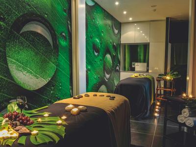 Sala de bienestar oscura con camillas de masaje, decoración verde en la pared e iluminación suave.