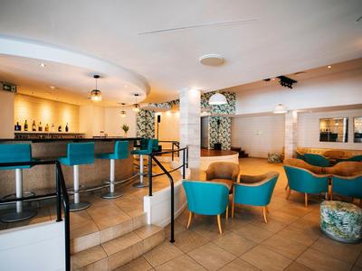 Bar elegante de hotel con sillones azules, sillas de madera y ambiente moderno con luz cálida.