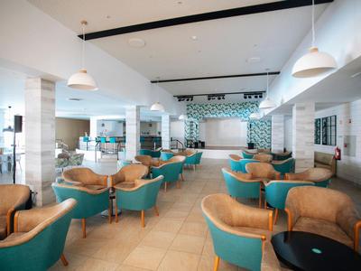 Amplia sala de estar luminosa con sillones turquesas y marrones bajo lámparas colgantes blancas.