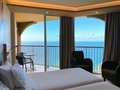 Habitación de hotel con dos camas y vista al océano a través de un balcón con sillas.