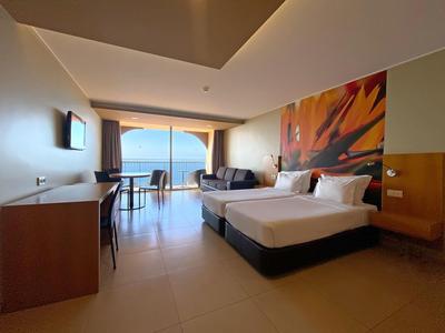 Habitación de hotel moderna con dos camas, escritorio y vista al mar a través de grandes ventanas.