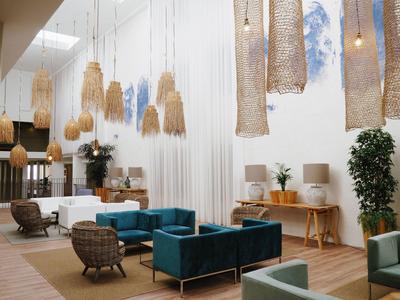 Área de lounge moderna en hotel con sofás azules, suelo de madera y lámparas colgantes de materiales naturales.