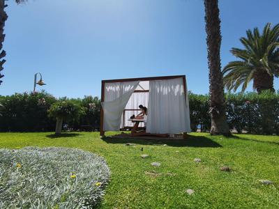 Jardín con césped verde, pabellón con cortinas y persona debajo, palmeras al fondo.