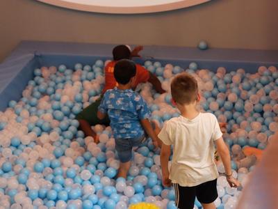 Kinder spielen in einem Ballbecken mit blauen und weißen Bällen in einem Innenraum.