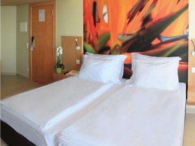 Dos camas individuales con sábanas blancas frente a una pared con un gran mural floral en una habitación de hotel.