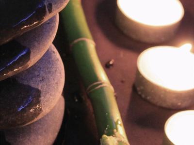 Piedras grises apiladas junto a bambú verde y velas pequeñas encendidas sobre superficie lisa.