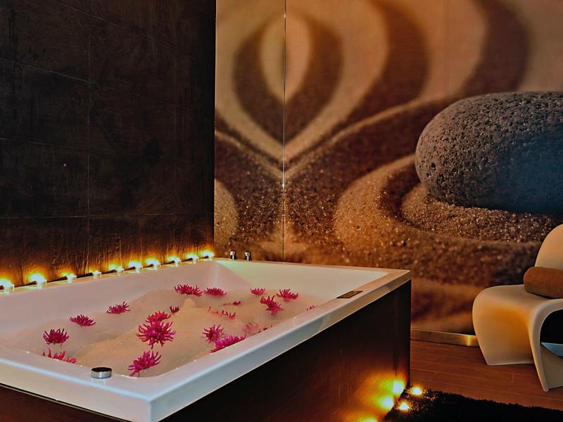 Un spa con bañera iluminada llena de flores y piedras relajantes en la pared.