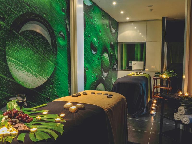 Sala de bienestar oscura con camillas de masaje, decoración verde en la pared e iluminación suave.