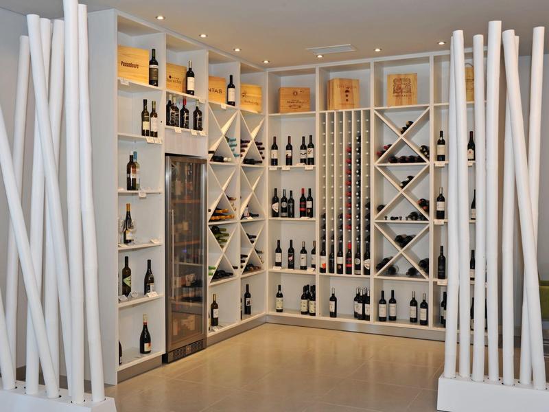 Bodega moderna con estantería blanca y varias botellas de vino en una esquina de la habitación.