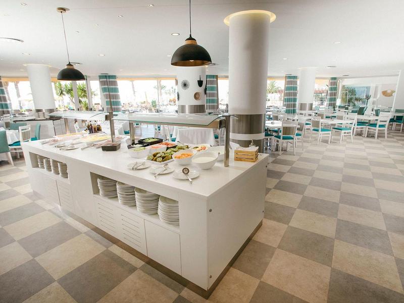 Restaurante moderno y luminoso con isla de buffet y muchas mesas frente a grandes ventanas.