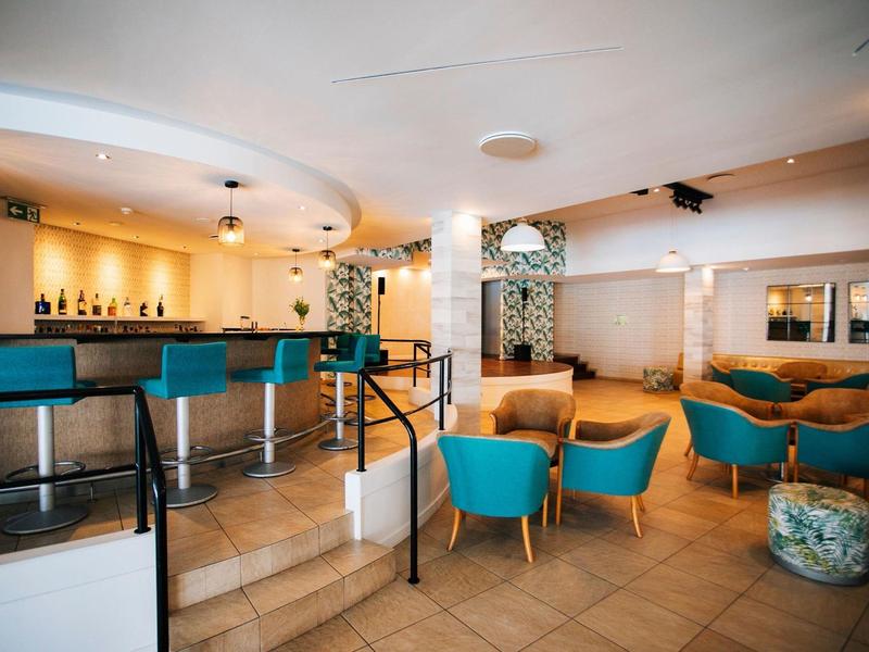 Bar elegante de hotel con sillones azules, sillas de madera y ambiente moderno con luz cálida.