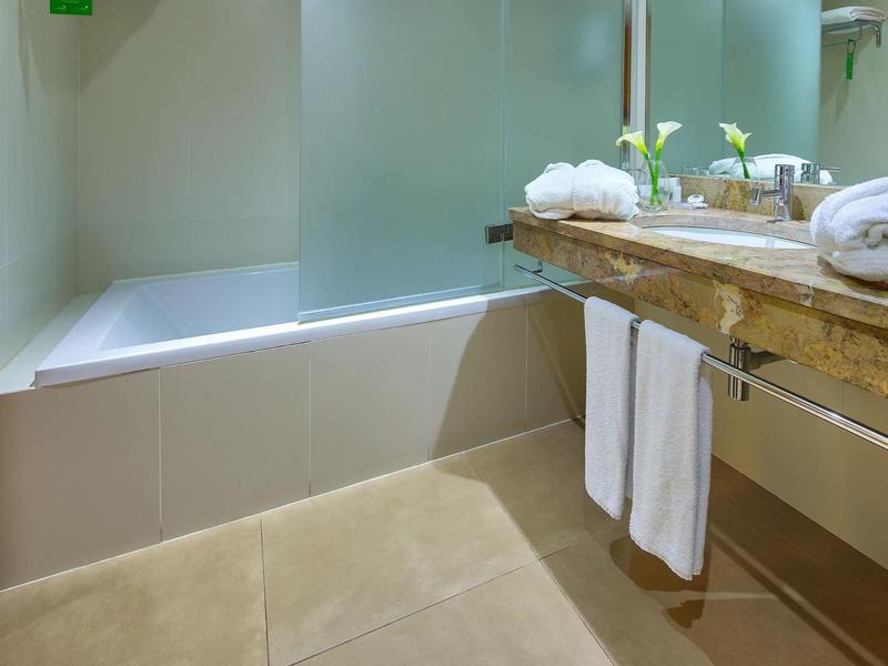 Baño luminoso con bañera, lavabo de madera y pared de vidrio esmerilado.