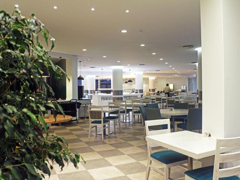 Área de restaurante de hotel moderno con sillas y mesas blancas, bien iluminada y espaciosa.