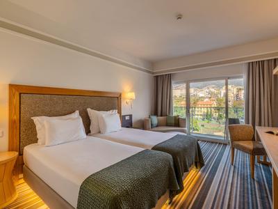 Modernes Hotelzimmer mit zwei Einzelbetten, Sitzbereich und Blick auf eine Terrasse mit Berglandschaft.