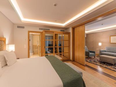 Modern eingerichtetes Hotelzimmer mit Bett, Sitzecke und warmweißer Beleuchtung.
