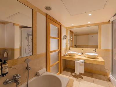 Helles Badezimmer mit Badewanne, zwei Waschbecken und Dusche in warmen Beige- und Holztönen.