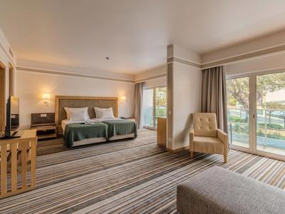 Geräumiges Hotelzimmer mit Doppelbett, Stuhl, Fernseher und Blick auf Pool und Garten.