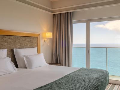 Modernes Hotelzimmer mit Doppelbett und Meerblick durch große Glasfenster.