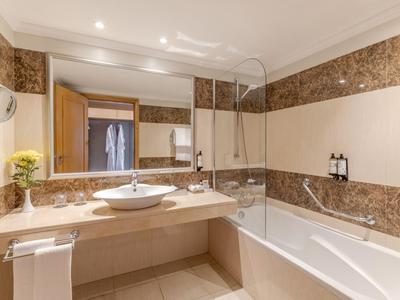Modernes Hotelbad mit Marmorakzenten, Wanne, Waschbecken und großen Spiegeln.