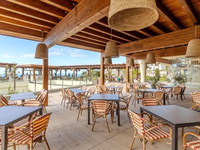 Offener Speiseraum mit Holzdach und Bambuslampen in einem Hotel, mit Blick auf den Sandstrand.