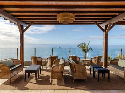 Hotelterrasse mit Sitzgruppen unter Holzdach mit Blick auf das Meer und Himmel.