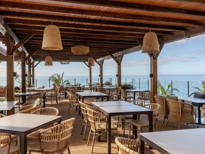 Freiluft-Restaurant mit Holzbalkendecke und Meerblick, ausgestattet mit Tischen und Stühlen aus Rattan.