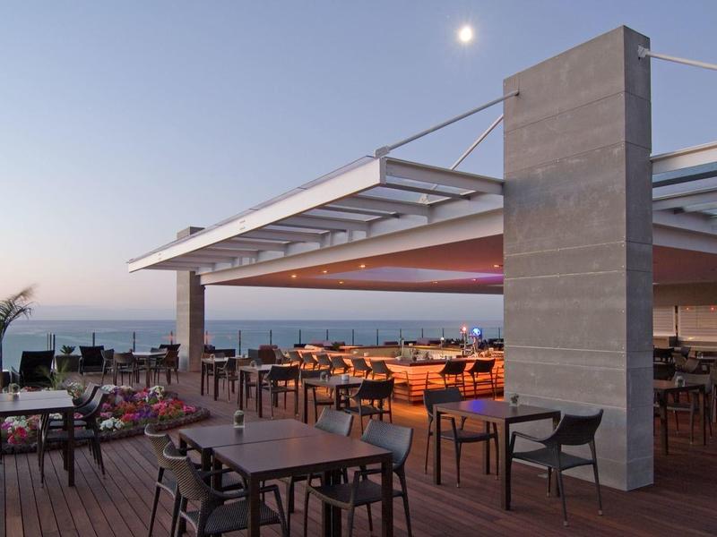 Moderne Dachterrasse mit Holzboden, Sitzgruppen aus Holz, Meerblick und hellem Abendhimmel.