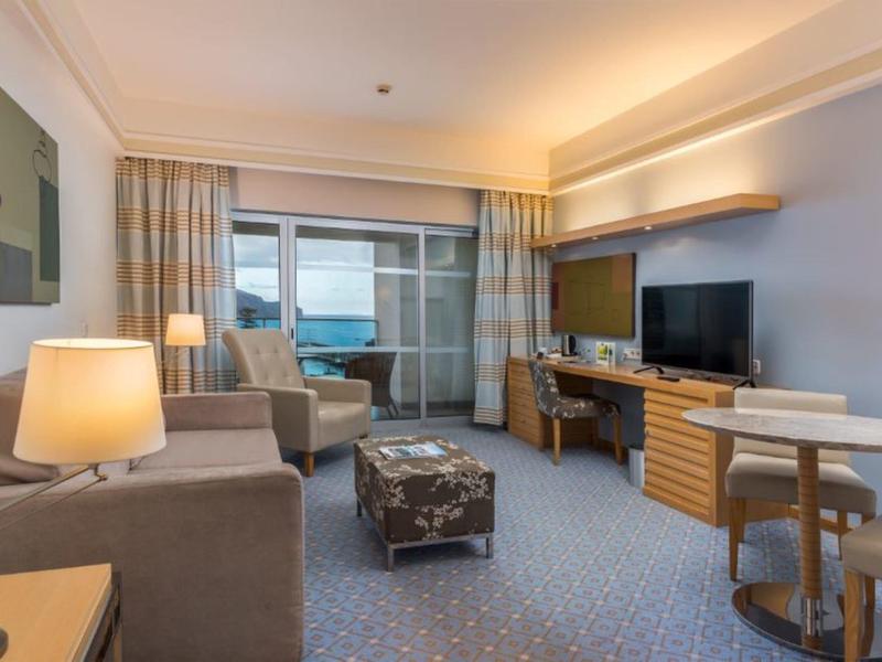 Moderner Wohnbereich mit Sofa, Sessel, TV, Schreibtisch und Balkon mit Meerblick.