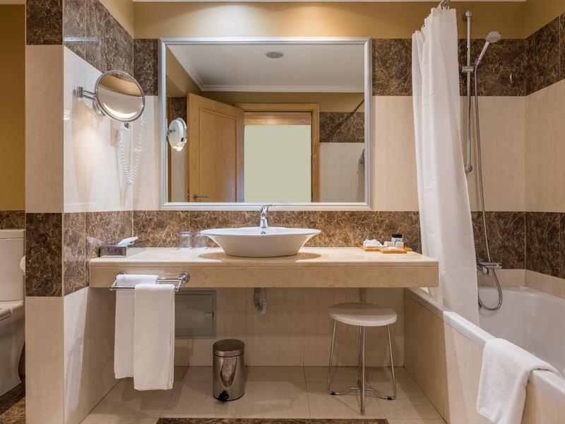 Helles Badezimmer mit großem Spiegel, moderner Waschtischschale, Badewanne und weißen Handtüchern.