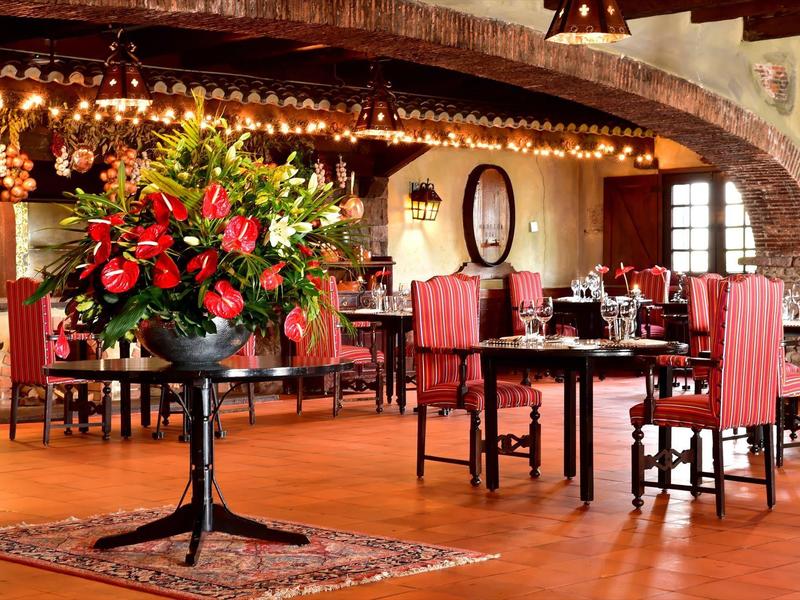 Rustikaler Speisesaal mit Holztischen, roten Stühlen und großem Blumenarrangement in Vase.