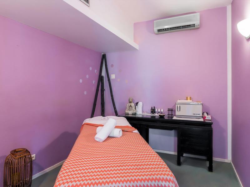 Kleiner Raum mit lila Wänden, Massageliege, schwarzem Schreibtisch und entspannter Atmosphäre.