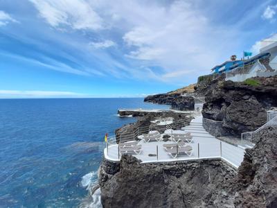 Terrasse mit Tischen und Stühlen auf Felsen über klarem Meer und blauem Himmel
