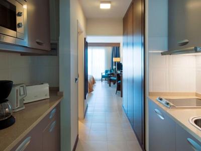 Blick durch einen modernen Hotelflur zu einem hellen Zimmer mit großer Fensterfront.