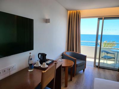 Moderner Hotelraum mit Stühlen, Tisch, Wasserflasche und Balkon mit Meerblick