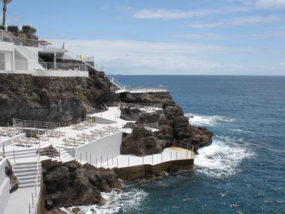 Hotelterrassen und Treppen führen zu einem Steilufer mit Blick auf das blaue Meer.