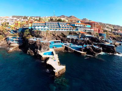 Hotelanlage auf felsiger Küste mit mehreren Pools und Blick auf das blaue Meer.