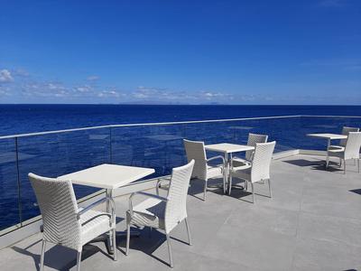 Offene Terrasse mit weißen Tischen und Stühlen vor dem blauen Meer