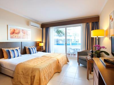 Helles Hotelzimmer mit Doppelbett, Sitzecke und Zugang zu einem Balkon mit Blick.