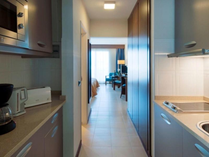 Blick durch einen modernen Hotelflur zu einem hellen Zimmer mit großer Fensterfront.