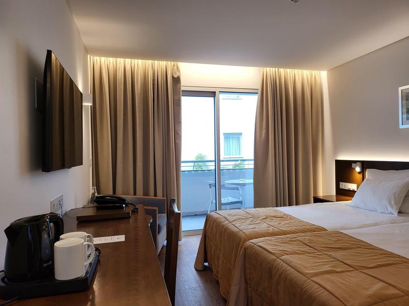 Gemütliches Hotelzimmer mit Doppelbett, TV, Schreibtisch und Balkon mit Blick auf den Pool.