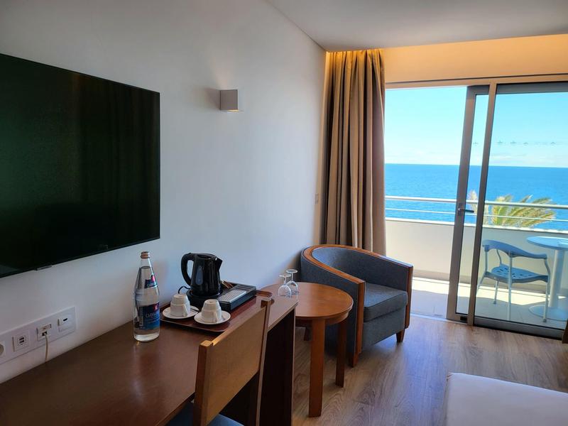 Moderner Hotelraum mit Stühlen, Tisch, Wasserflasche und Balkon mit Meerblick